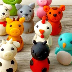 there are many small toy animals on the wooden table, all different colors and sizes