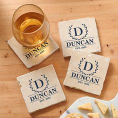 four personalized coasters and a glass of beer on a wooden table with cheese