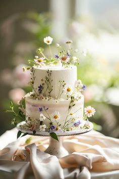 a white wedding cake with flowers on it sitting on a table in front of a window