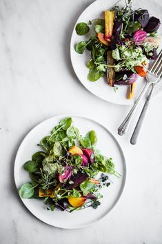 two plates filled with salad on top of a white table