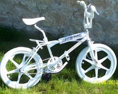 a white bicycle sitting in the grass next to a stone wall