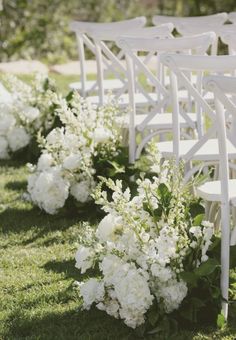 rows of white chairs with flowers lining the aisle for an outdoor wedding ceremony in the grass