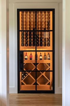 a wine cellar in the corner of a room with wooden floors and black glass doors