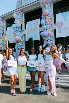 some pretty young ladies standing in front of a building with balloons on the side of it