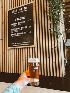 a person holding up a beer glass in front of a wall with a menu on it