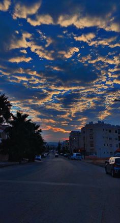 the sun is setting behind some clouds in the sky over a street with parked cars and palm trees