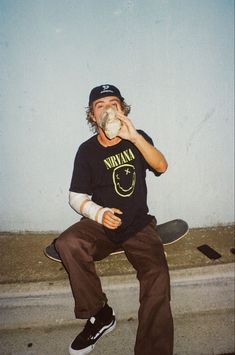 a man sitting on top of a skateboard while drinking from a cup in his hand