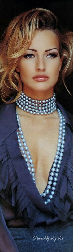 a woman with blonde hair wearing a blue dress and pearls on her neck, posing for the camera