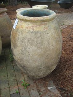 two large vases sitting next to each other on a brick walkway in front of trees