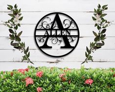 a sign that says allen on it in front of some bushes and flowers with pink flowers