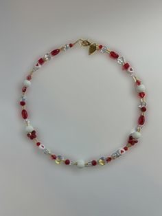 a red and white beaded necklace with gold accents on a gray background, featuring a heart charm