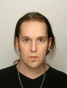 a man with long hair wearing a black shirt and silver chain around his neck is looking at the camera