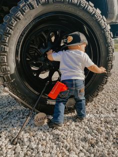 a little boy standing next to a big tire