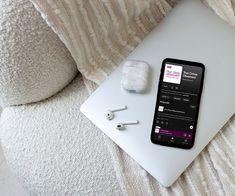 an open laptop computer sitting on top of a white couch next to earbuds