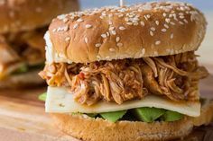 a pulled pork sandwich with cheese and lettuce on a cutting board next to another sandwich