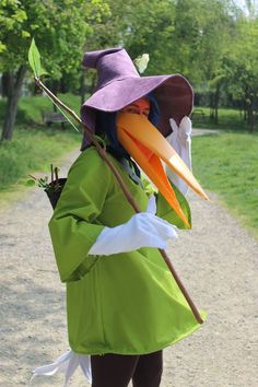 a woman dressed in green and purple is holding a stick with two large birds on it