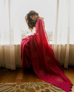 a woman in a red dress sitting on a window sill looking out the window