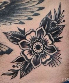 a black and white flower tattoo on the back of a man's chest, with wings