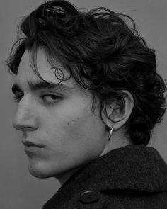 a black and white photo of a young man with curly hair wearing earrings