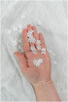 a person's hand holding some white flowers on top of a lace covered surface