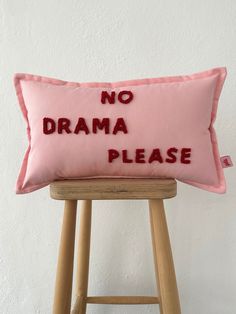 a pink pillow with the words no drama please embroidered on it sitting on a stool