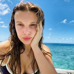 a beautiful young woman sitting on top of a boat in the ocean with her hands to her face