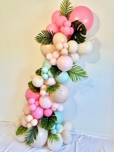 the balloon arch is decorated with palm leaves and pink, blue, and white balloons