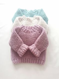 three knitted sweaters sitting next to each other on top of a white surface