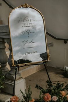 a sign that is sitting on the ground with flowers in front of it and a sky background