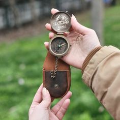 a person holding a small pocket watch in their left hand and a leather case on the other