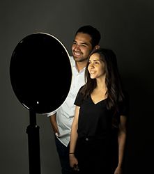 a man standing next to a woman in front of a black background holding a camera