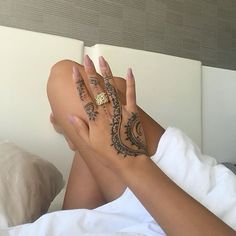 a woman laying on top of a bed holding her hands up to her face with hendi tattoos