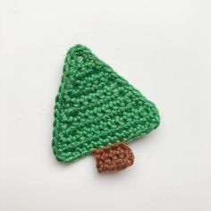 a crocheted green christmas tree ornament on a white surface with a brown base