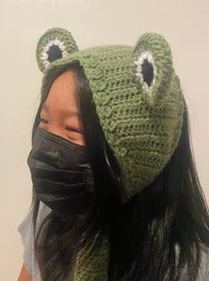 a woman wearing a green frog hat and black mask covering her face with a scarf