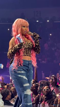 a woman with pink hair is on stage and holding a microphone in her hand while people are watching