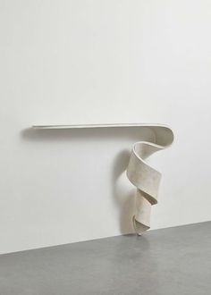 a white sculpture sitting on top of a cement floor next to a wall mounted shelf