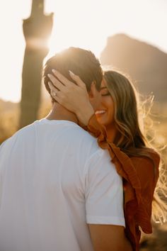 a man and woman embracing each other in front of a saguado cactus at sunset