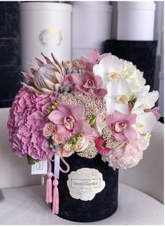 a black vase with pink and white flowers in it sitting on a table next to some containers