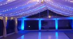 a white dance floor with blue lights and drapes on the ceiling is lit up