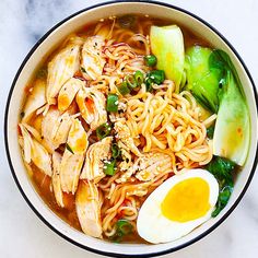 a bowl filled with noodles, meat and vegetables next to an egg on the side