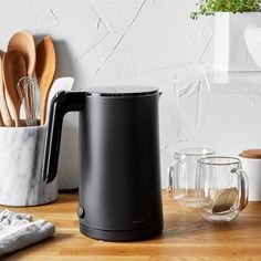 a black coffee pot sitting on top of a wooden table next to utensils