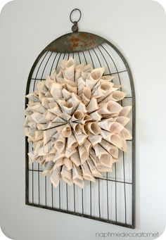 an old book page wreath is hanging on a metal rack with a birdcage