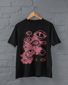 Thanks for stopping by! Goth Eyes T-shirt Printed on a super soft, cotton tee Dispatched in 5 working days or sooner Unisex Free UK delivery Material: 100% ringspun cotton. Chest (to fit): S  34/36   M  38   L  40/42   XL  44/46   XXL  48/50 ECO-FRIENDLY Each garment is made to order, reducing extra material and energy that would be otherwise wasted We use DTG printing process which is easier on the environment than screen-printing Our ink is bright and also eco-friendly. Do not tumble dry. Wash Emo Crew Neck T-shirt With Graffiti Print, Edgy Pink T-shirt With Graphic Print, Alternative Style Funny Print Crew Neck Tops, Alternative Funny Print Crew Neck Tops, Alternative Style Pink Tops With Graphic Print, Alternative Cotton Tops With Funny Print, Alternative Cotton Top With Funny Print, Funny Print Cotton Top In Alternative Style, Pink Grunge T-shirt With Screen Print