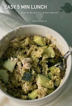 a white bowl filled with rice and cucumbers on top of a table next to an apple