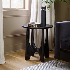 a living room with a chair, table and vase on the floor in front of a window