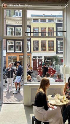 two women sitting at a table in front of a window with people standing around it