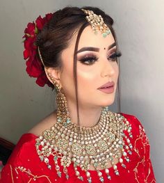 a woman wearing a red outfit with gold jewelry on her head and flowers in her hair