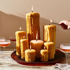 a person lighting candles on a plate with wine glasses in front of it and another hand reaching for the candle