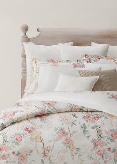 a bed with white sheets and pink flowers on the comforter, along with pillows