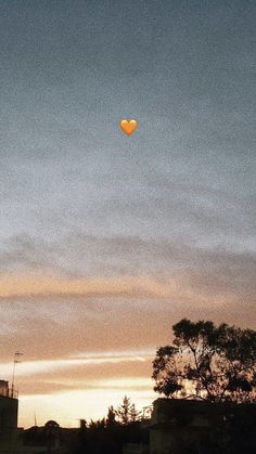 an orange heart shaped balloon is flying in the sky at sunset or dawn over some buildings